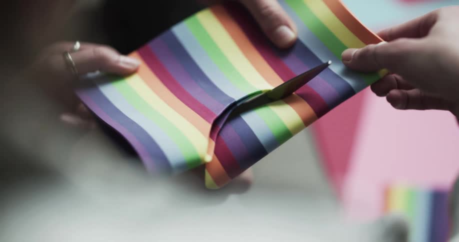 Two people cutting a piece of colorful paper using scissors