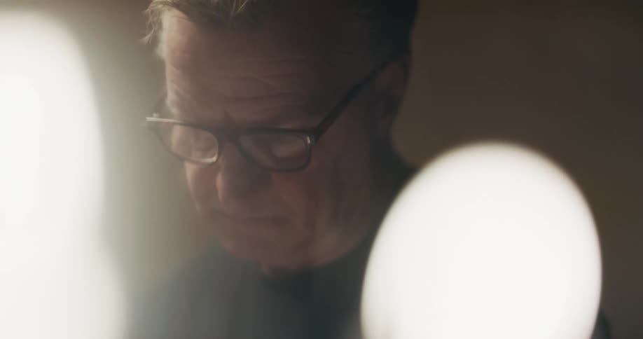 A man is standing indoors and wearing glasses
