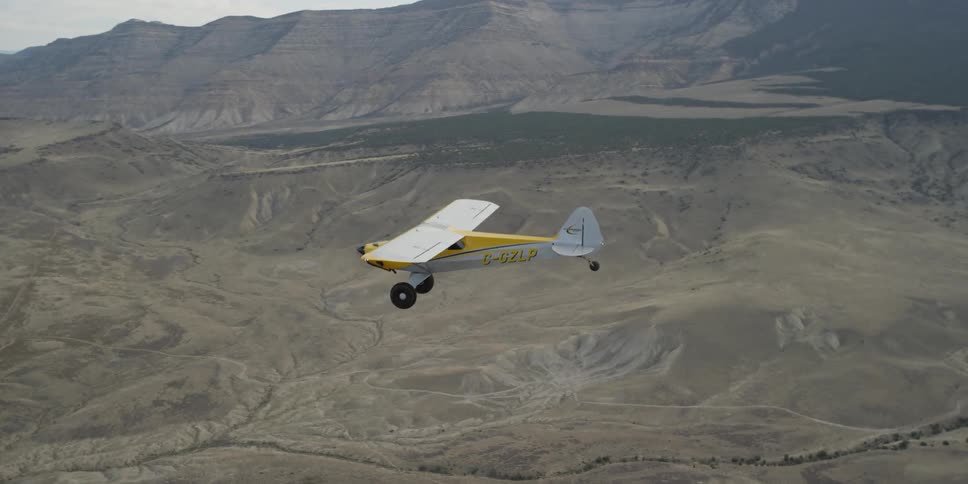 A yellow airplane flies over mountains and valleys