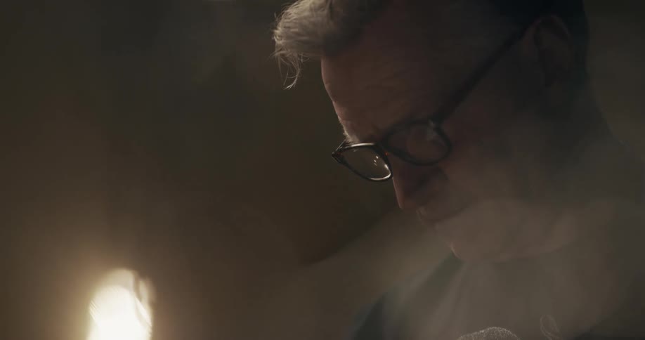 A man wearing eye glasses standing in a room looking down