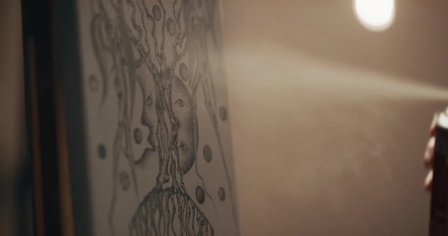 A person uses a spray can to spray an illustration resting an easel indoors