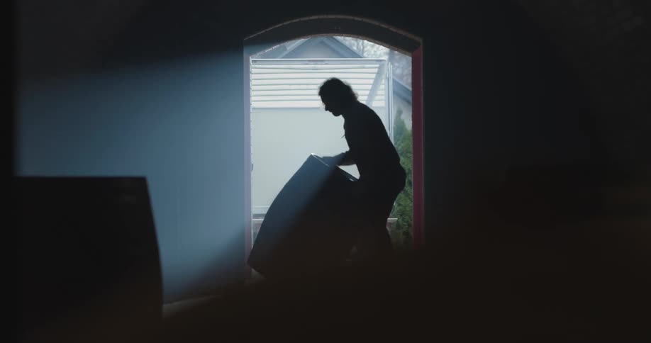 A silhouette of a person rolling a barrel in a room through a doorway