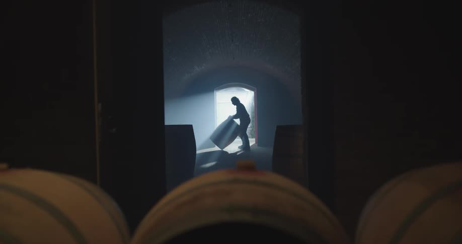 A man rolling a wood barrel into a dark cellar