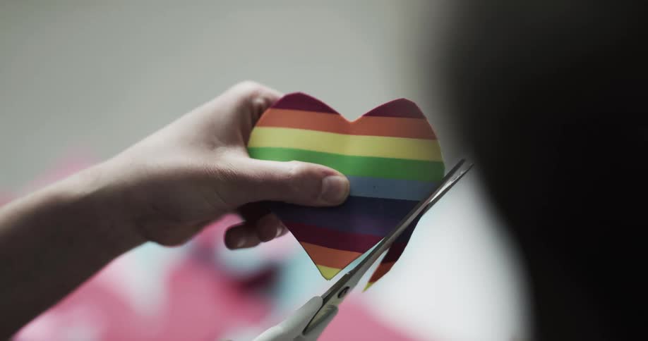 A woman smiles as she cuts a heart shape on rainbow printed paper