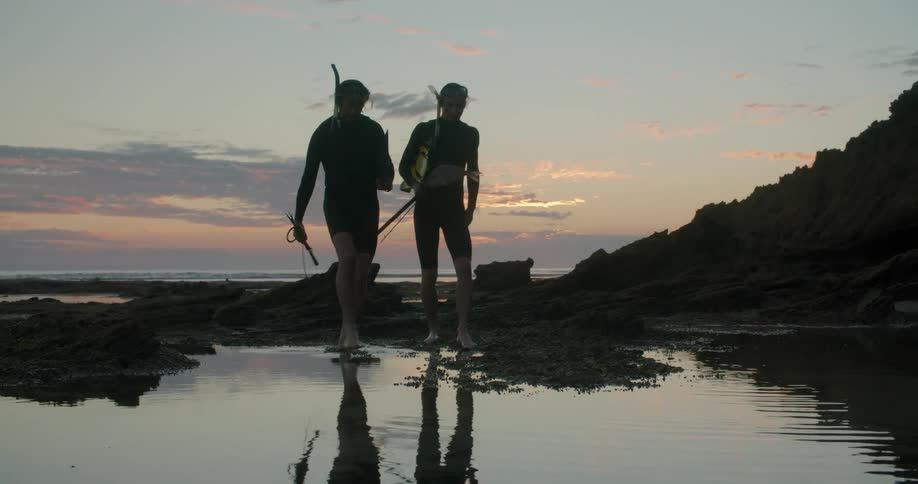 Two men on a fishing trip walk over the jagged rocks near the coast at sunset