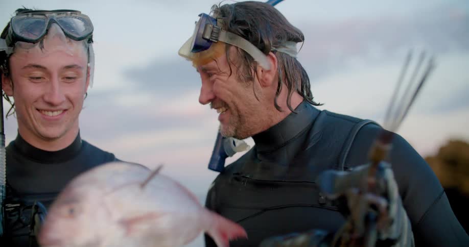 Two men laugh and hug as they admire a fish they caught while spearfishing and snorkeling