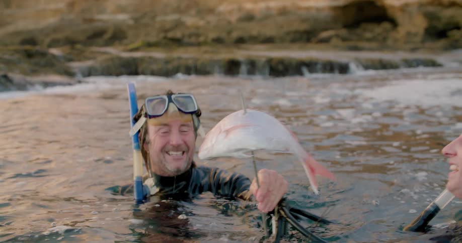 Two men smiling and high fiving after spearing a fish in ocean water