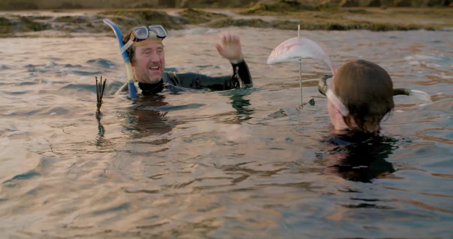 A man and teenager high five each other in the water with a speared fish