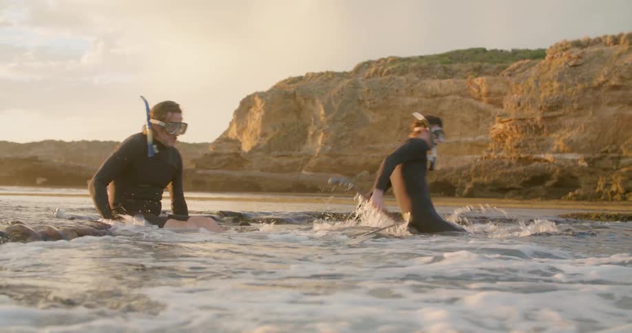 A father and son wearing snorkeling equipment ease into the water as they go spear fishing