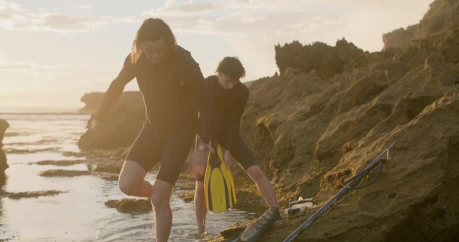 A father and son sit on the shore and then picks up their fins