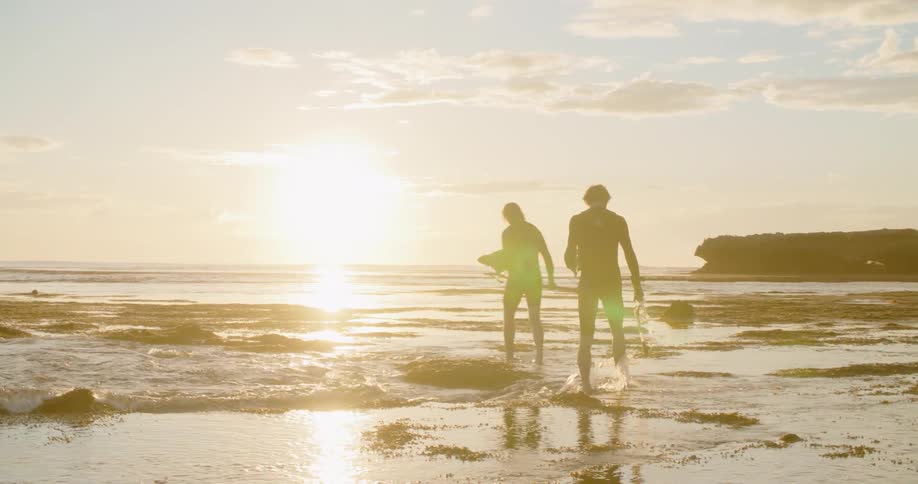 A silhouette of two men on a beach with the sky and clouds in the background