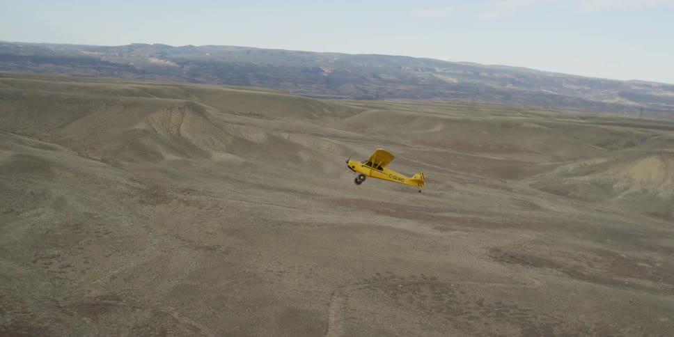 A small yellow airplane takes off over a desert