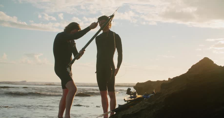 Two men with a fishing spear stand on the shore