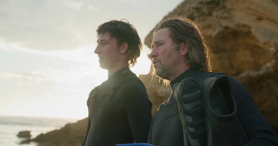 Two men with scuba gear on a beach with the sky and clouds in the background