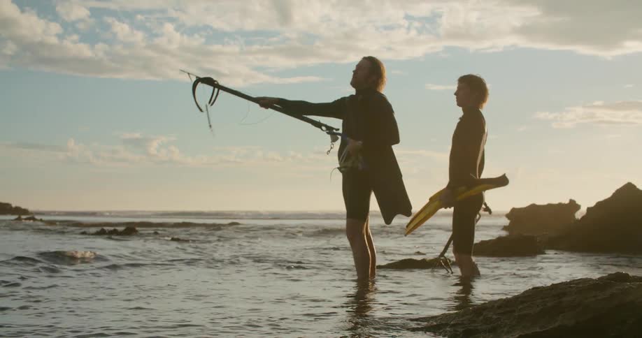 A father and son walk in to the water carrying fishing gear