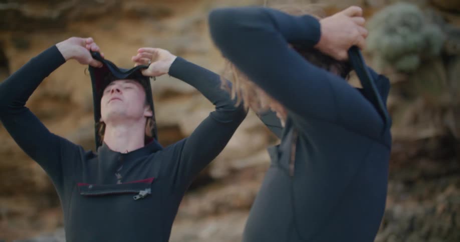 Two men putting on surfing suits outdoors during the day