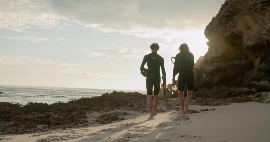 A father and son walk down the beach carrying scuba gear