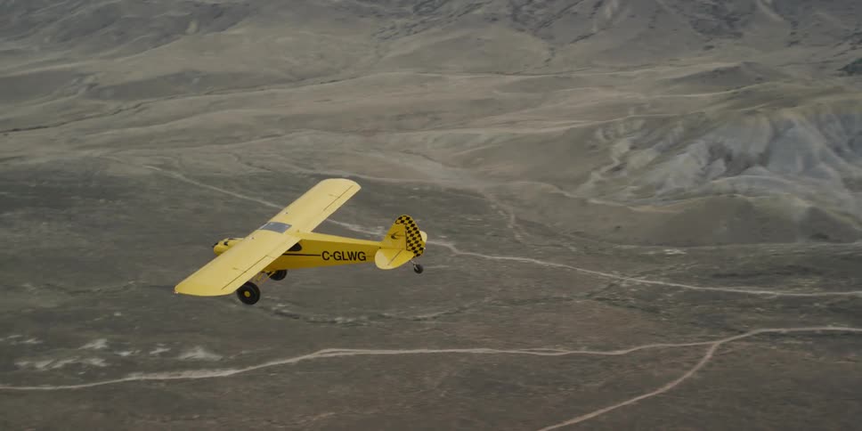 Small yellow airplane soaring above the brown ground