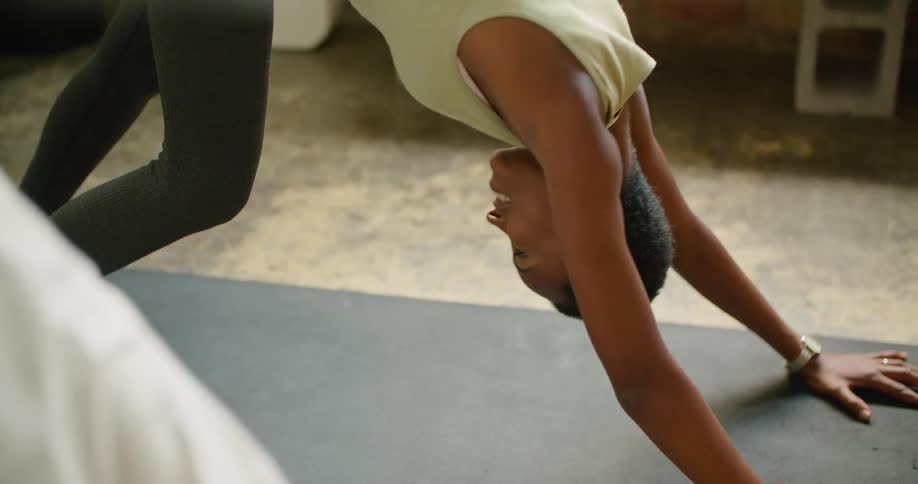A woman in a room on a mat on the floor stretching with a wall in the background