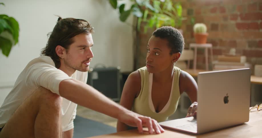 A man and woman sit together while looking at something on a laptop before coming to an agreement