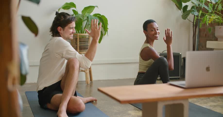 A man and a woman in a room on the floor stretching and looking at a laptop with plants and a wall in the background