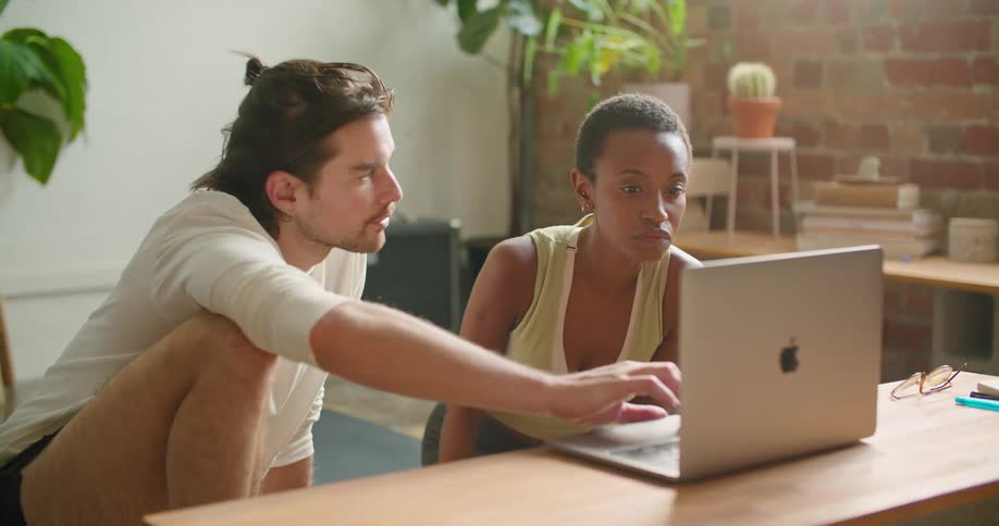 A man and woman sit on the floor while looking at a laptop screen together
