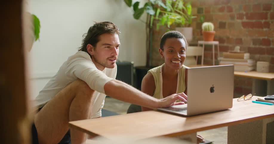 A man and woman view a laptop together while sitting on the floor of house during the day