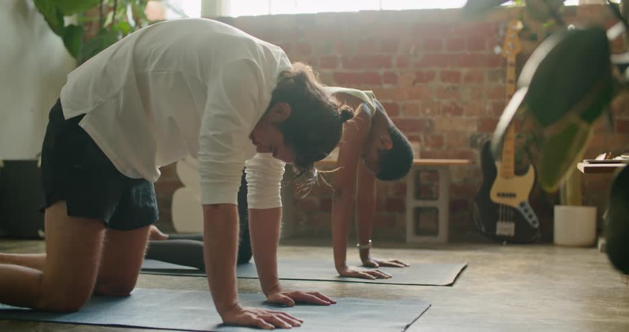 A man and a woman in a room on the floor stretching with plants and a wall in the background