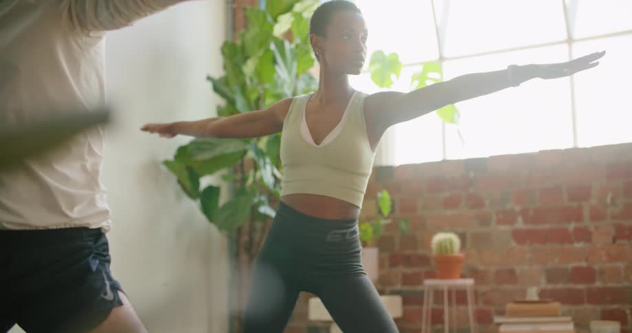 A man and woman move from a warrior pose to a triangle pose while doing yoga at home
