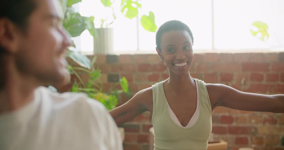 A man and woman perform yoga exercises together indoors and smile at each other
