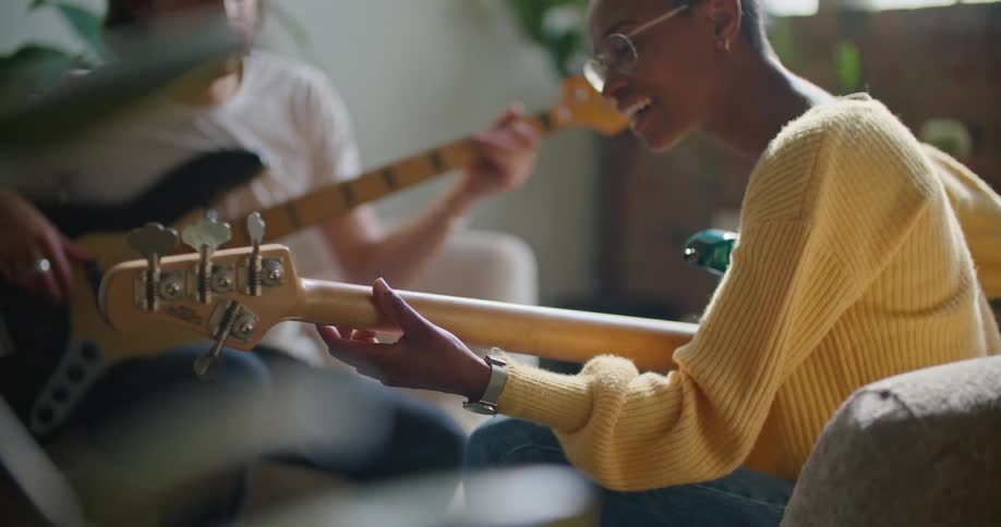 A man and woman play their guitars together in the living room of a house during the day