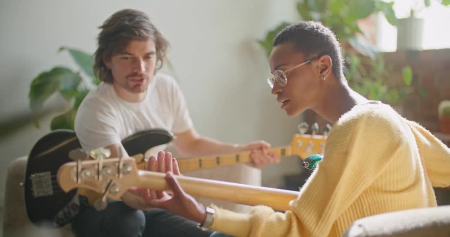A man teaches a woman how to play guitar as they sit facing each other