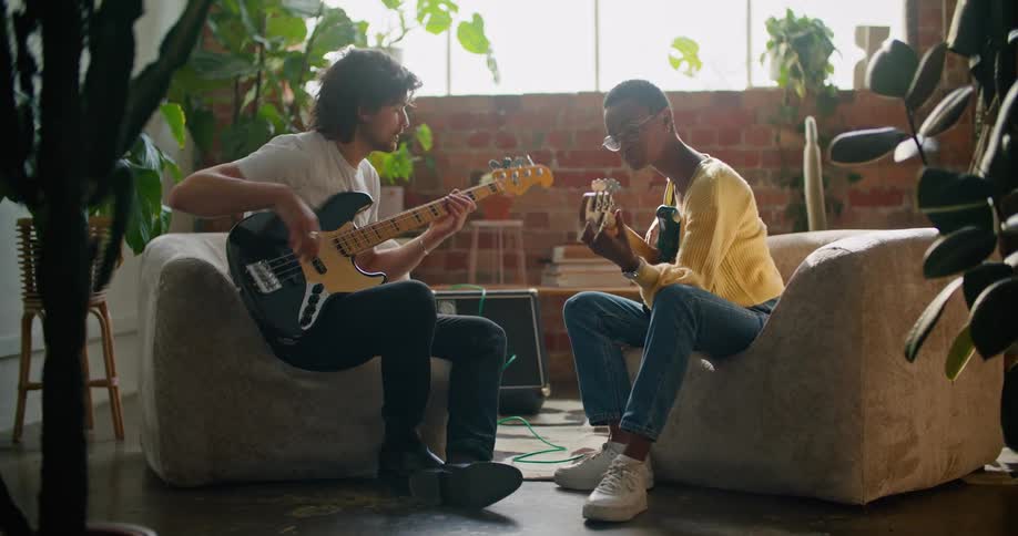 A man and a woman in a room sitting and playing guitars with a wall and window in the background