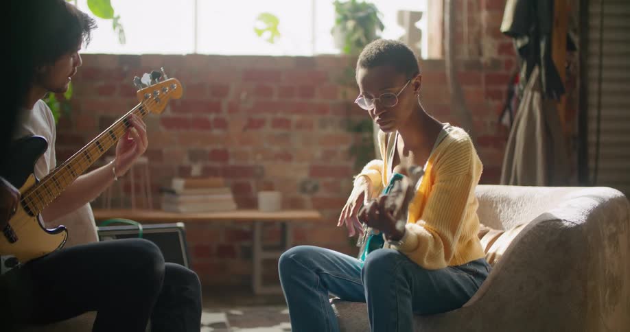 A man sits indoors and practices bass guitar with his female companion