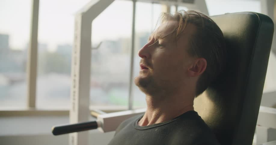 Man sitting on gym equipment straining trying to lift bars