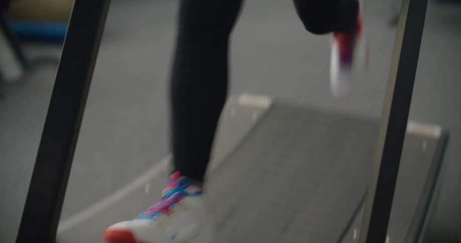 A man in a gym running on a treadmill with a wall and windows in the background