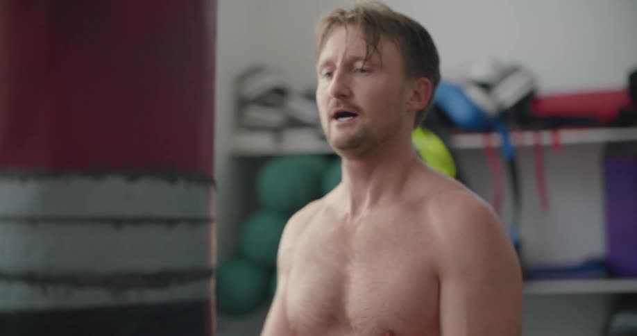 Man wearing boxing gloves hits bag before resting his head against it