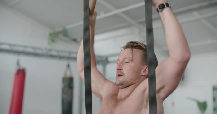 A man does pull up exercises on the steady rings in a gym