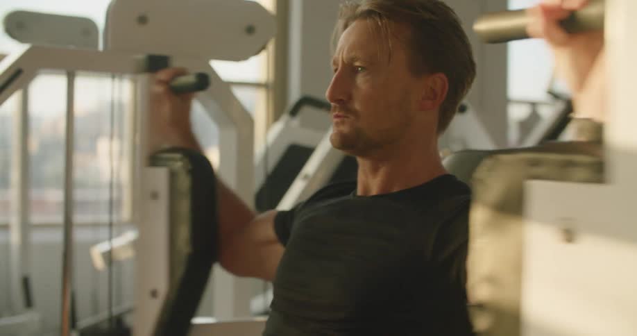 A man exercising on a exercising machine with equipment and windows in the background