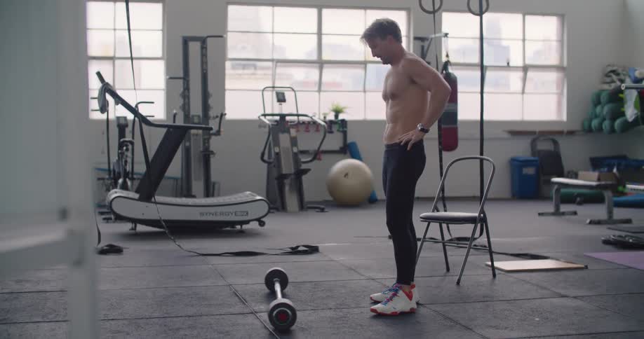 A man lifts a small weighted barbell as he exercises in a small fitness room