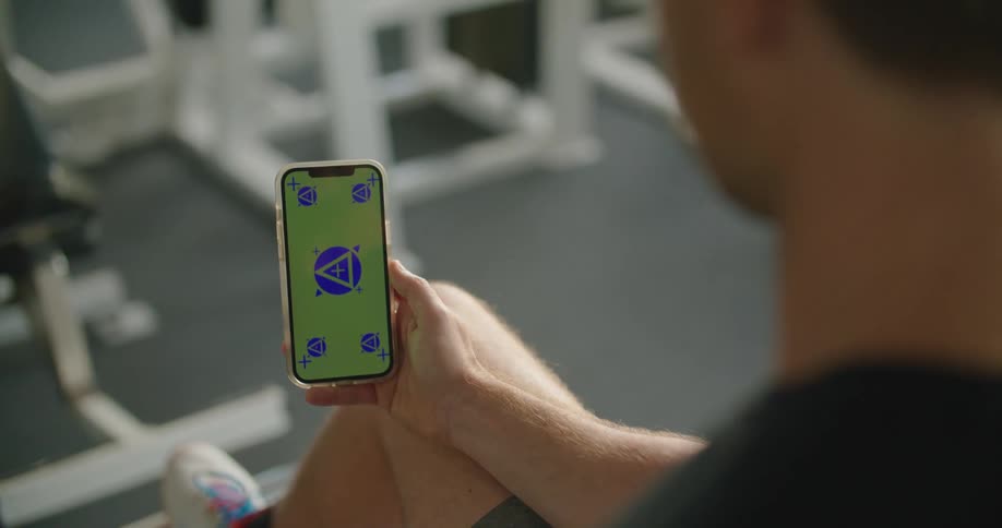 A man is in a gym and looking at his cell phone