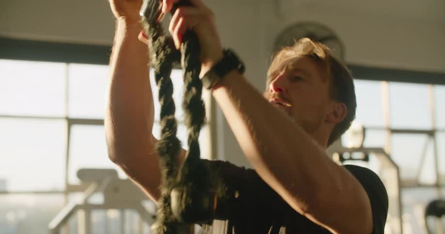 Man hanging weighted ropes from gym equipment at sunset