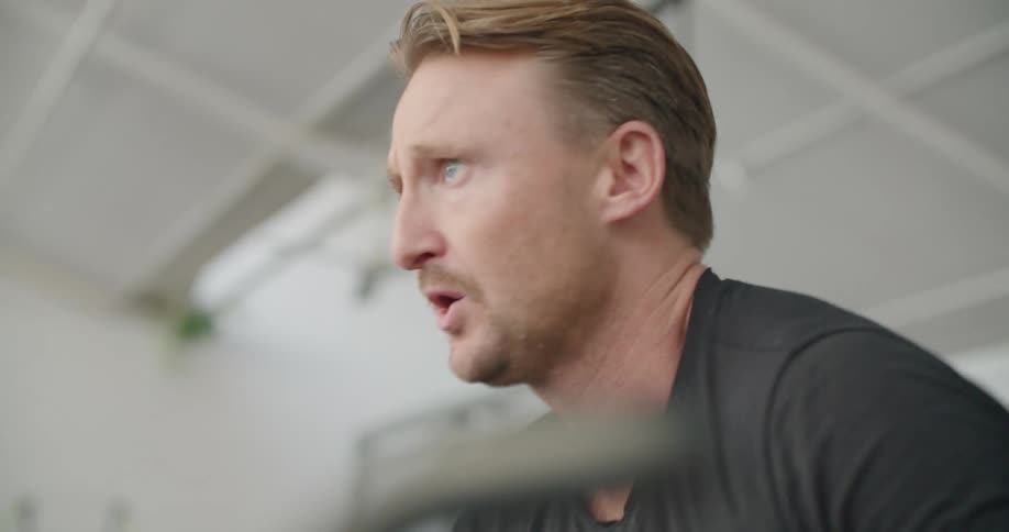 A man rides an exercise bike and stops to take a deep breath and check his watch