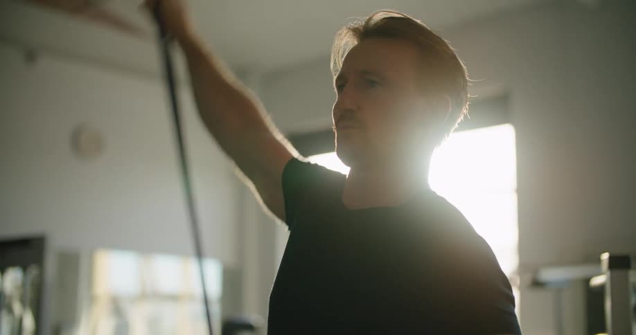 A man in a gym exercising with a wall and window in the background