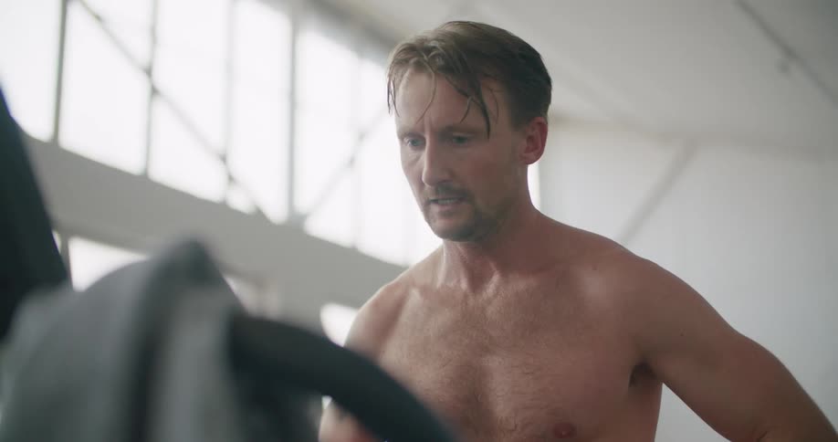 A man with a wristwatch standing on a treadmill with a wall and windows in the background