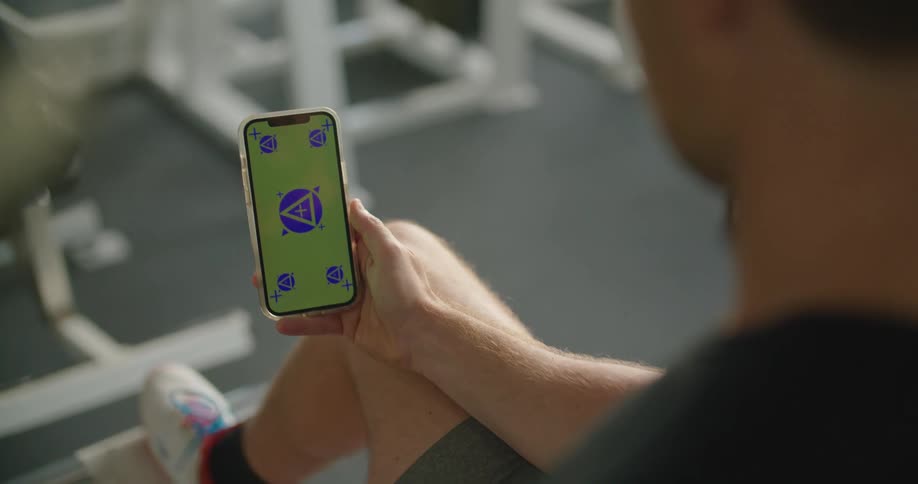A man sitting in a gym uses his thumb to scroll through information on his smart phone