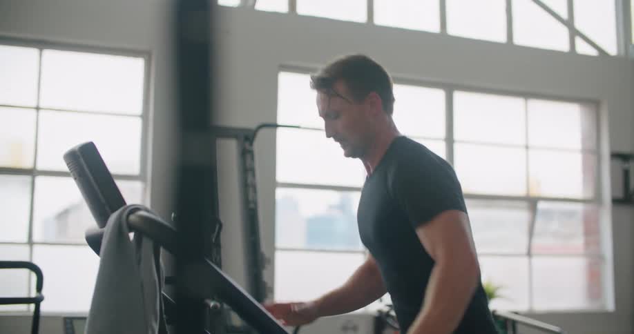 A man runs on a treadmill in a gym during the day