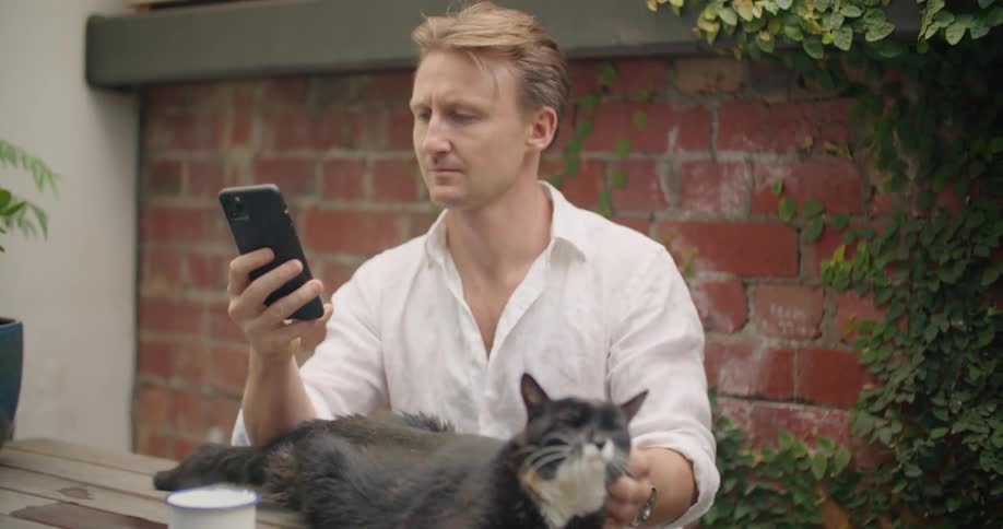 A man is petting his cat and sitting outdoors