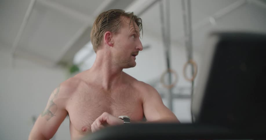Shirtless man catching his breath in a gym checks the our on his wristwatch