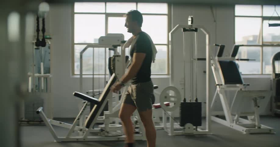 A man rests a towel on his shoulder as he walks through a fitness gym during the day
